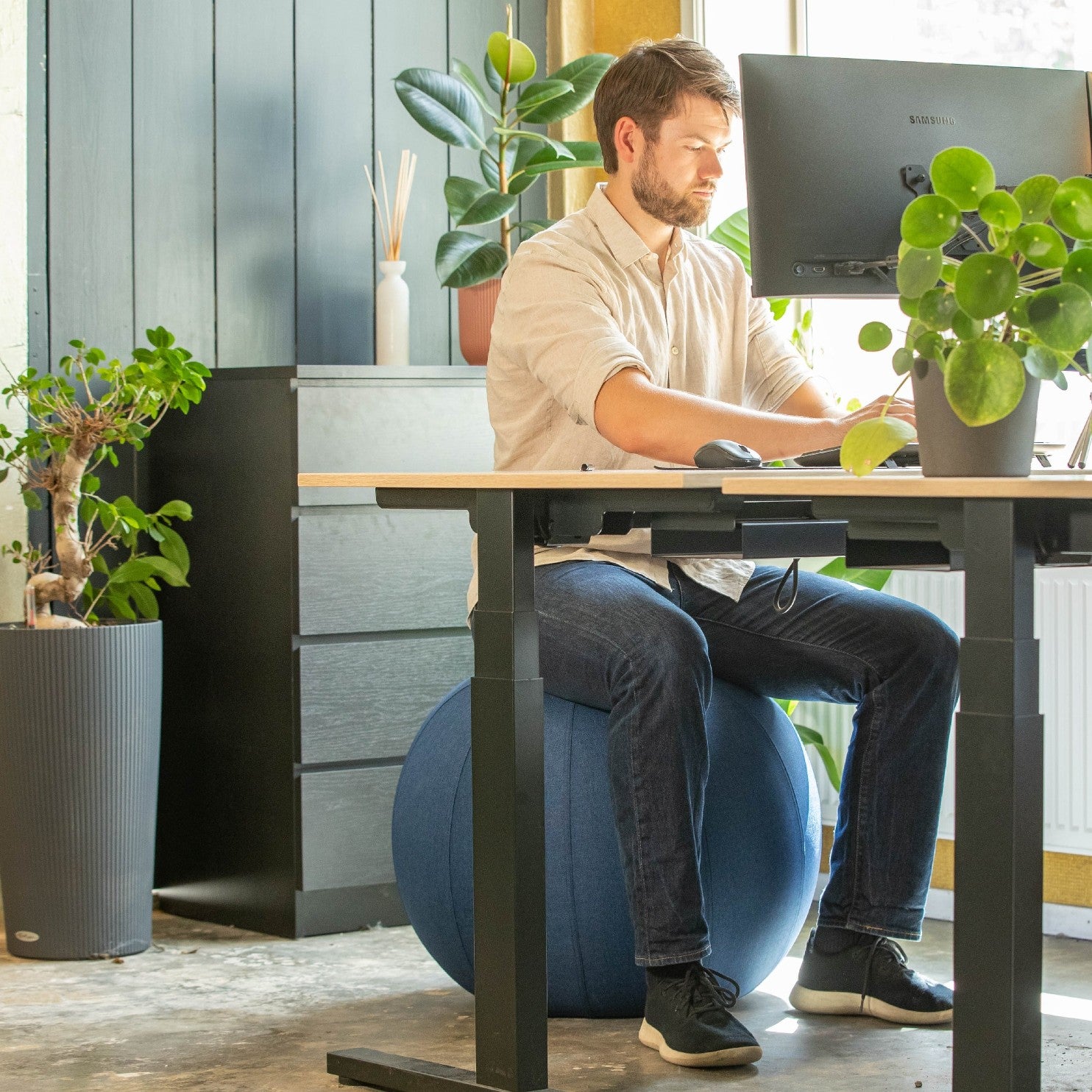 Een man op een linnen zitbal aan zijn bureau, genietend van een comfortabele en actieve werkhouding.