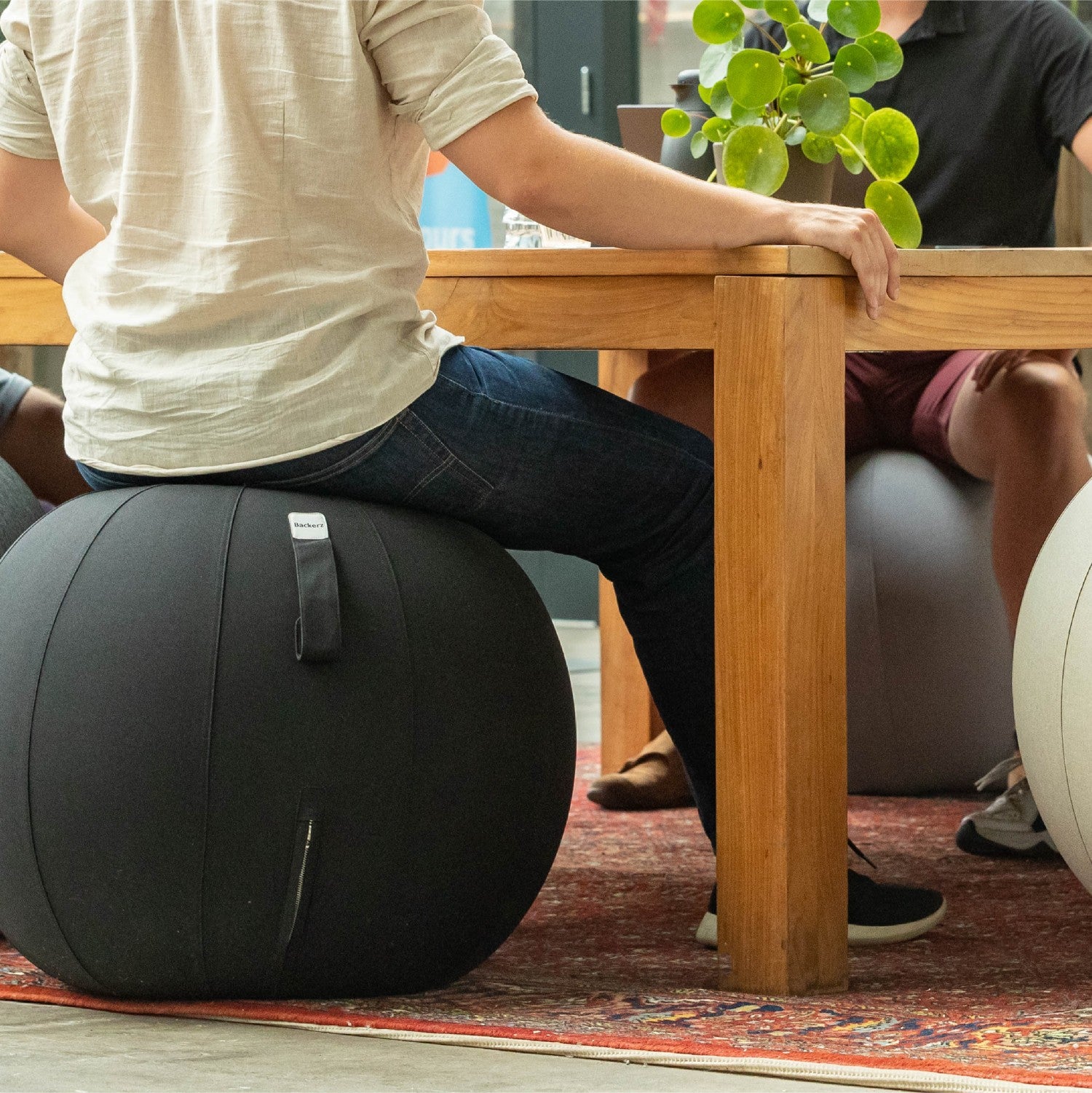 Twee mensen op een grote zitbal voor een tafel, een speelse en comfortabele sfeer in de ruimte.