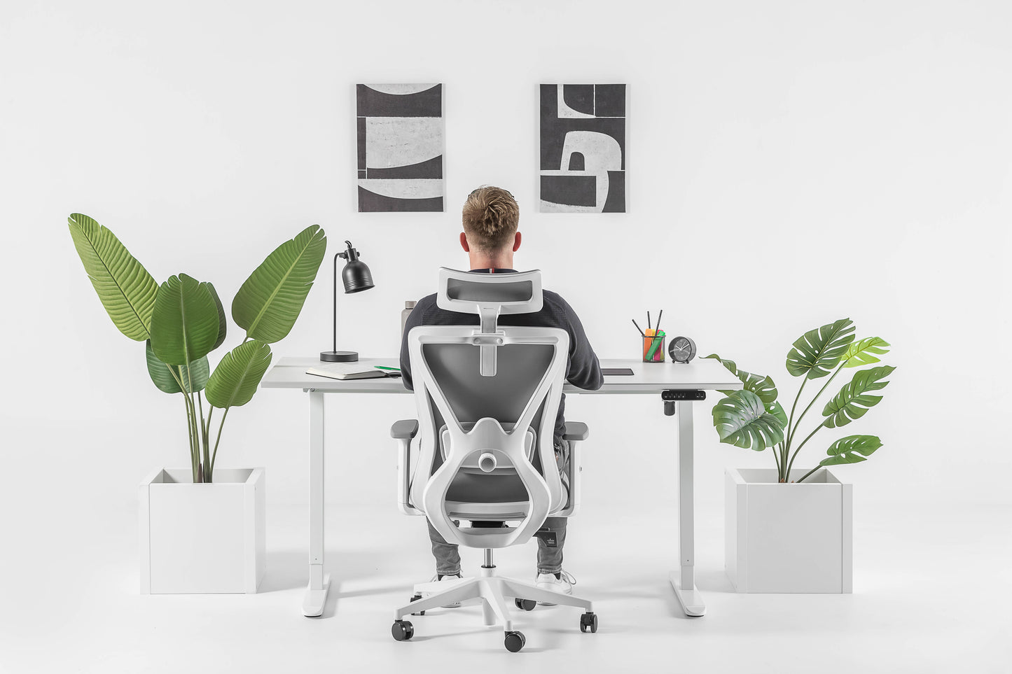 Een man aan een bureau met een plant ervoor, genietend van zijn werkplek in een moderne bureaustoel.