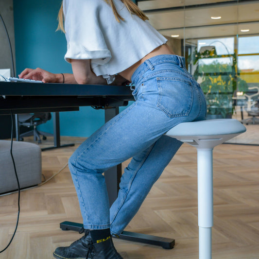 Een vrouw op een wiebelkruk aan een bureau, genietend van een comfortabele en duurzame werkplek.